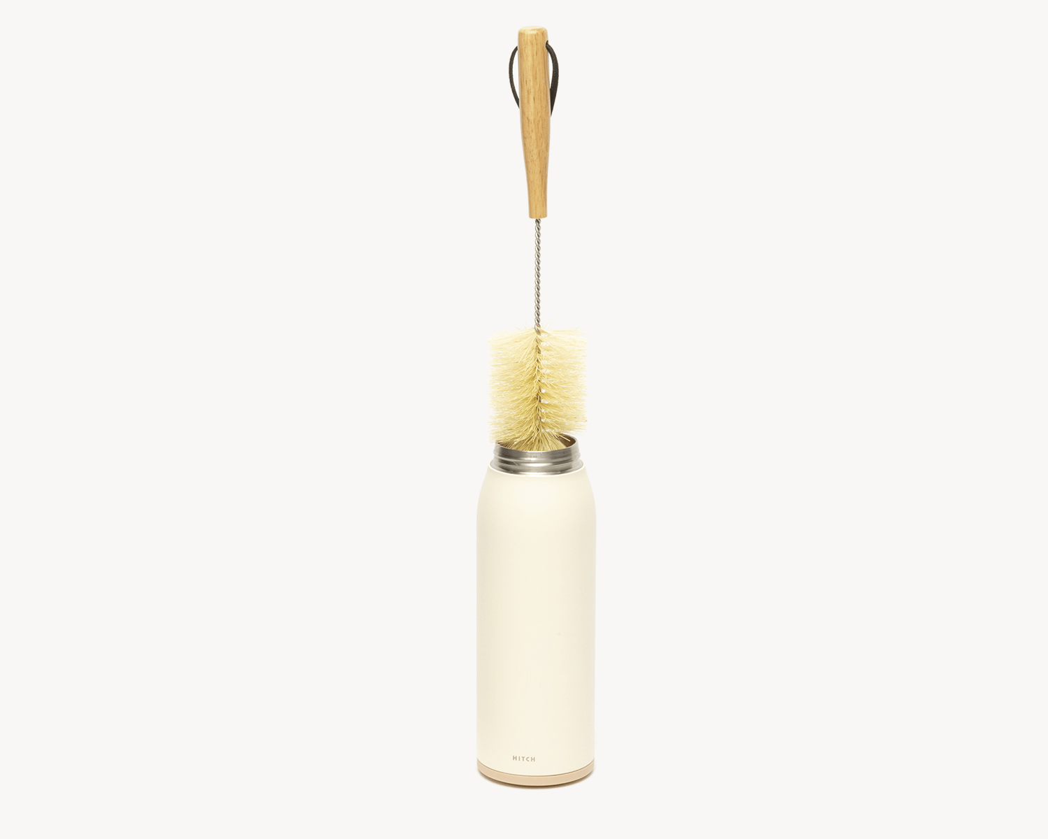 Hitch Bottle Brush with Natural Sisal Fibers, a stainless steel rod, and wooden handle inside Hitch Bottle and Cup in Natural White