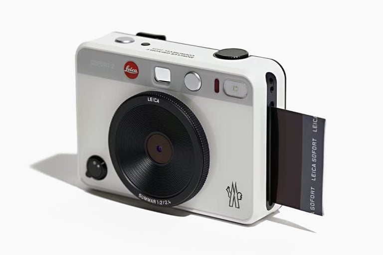 The Leica x Moncler Sofort 2 instant camera in white, featuring a sleek design with Moncler's logo and a black lens, printing an instant photo.