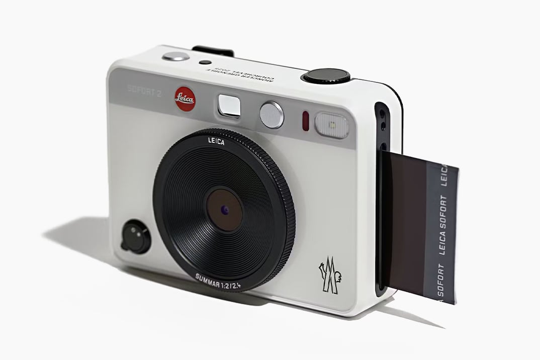 The Leica x Moncler Sofort 2 instant camera in white, featuring a sleek design with Moncler's logo and a black lens, printing an instant photo.